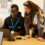 A student sat in front of a computer being supported by a tutor