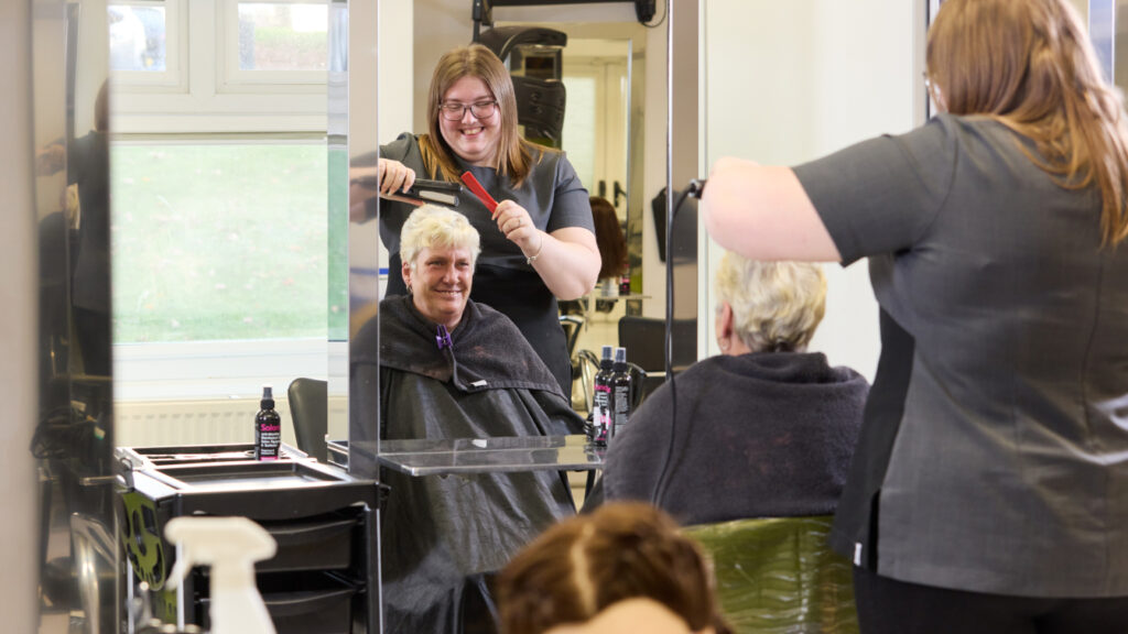 Photo of a hair and beauty student styling the hair of a woman in a hairdressing mirror