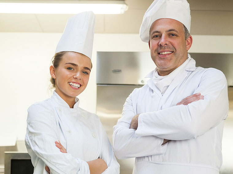 A student chef stands with her tutor cross armed.