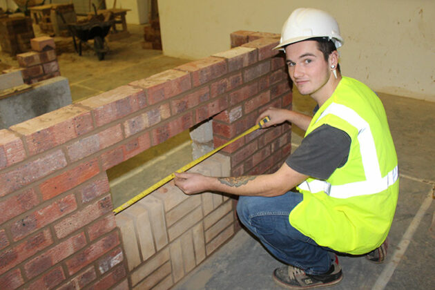 Nathan crouches next to his bricklaying work.