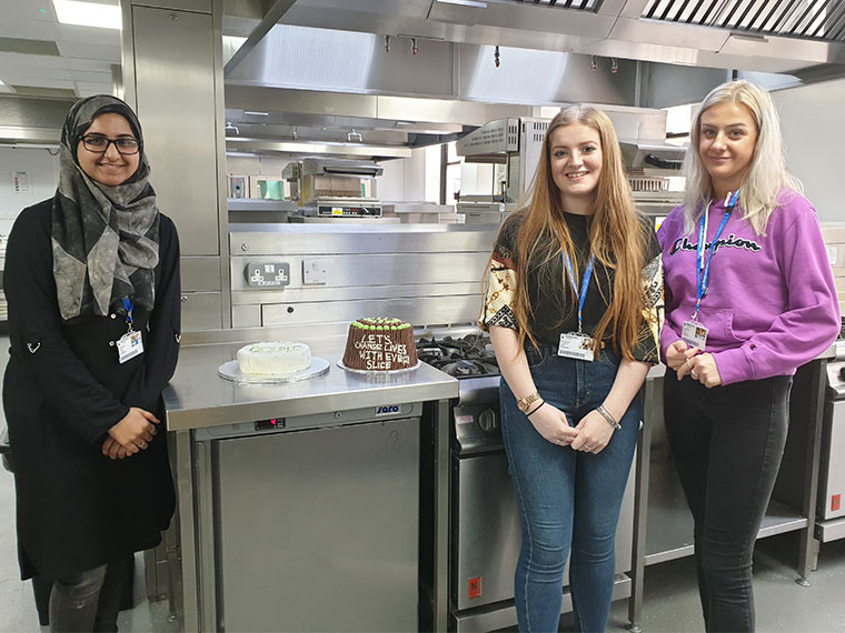 Student star bakers Minah, Charlotte and Lauren-Jade standing next to the cakes they've baked and designed to help raise funds for Macmillan.