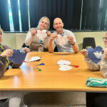Four people sat around a table holding up hearts that they have made