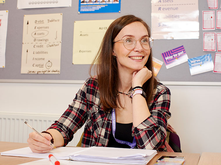 A smiling student sat at a table with a pen in their hand ready to write