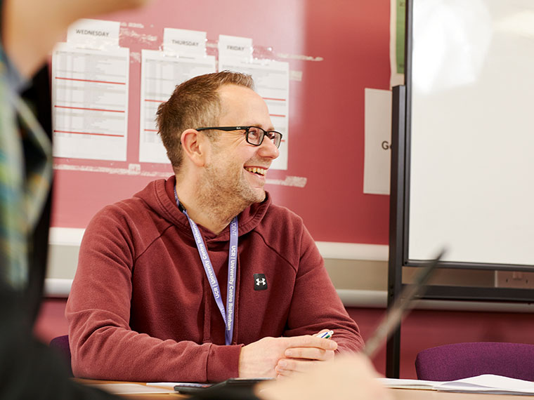 Someone sat at a desk smiling whilst looking away from the camera