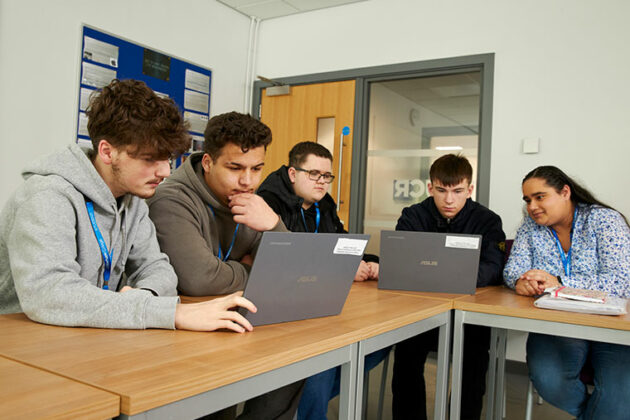 A group of students sat at a desk looking at laptops