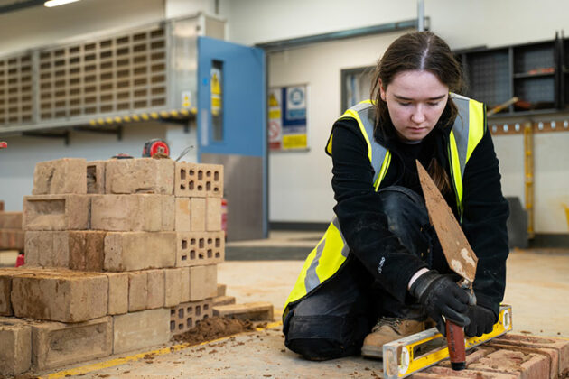 A student knelt down checking brick with a spirit level