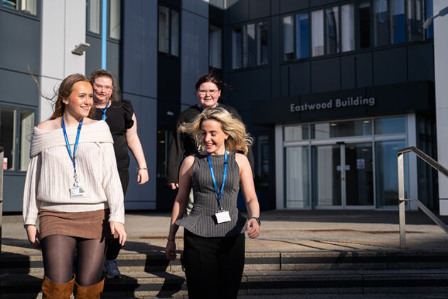 Four students smiling walking down the steps outside Rotherham College's Eastwood Building