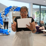 A female looking happy looking down at a piece of paper in her hands, a balloon arch in the background